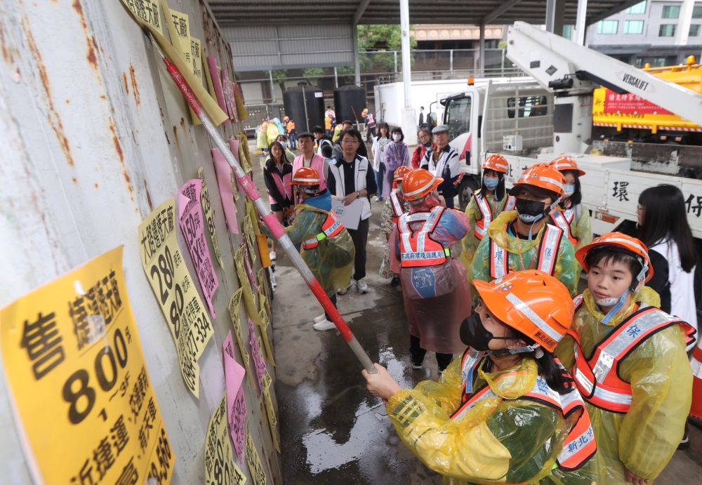 《圖說》清潔隊員的日常工作不僅要道路清掃和垃圾收運，其中包括刮除小廣告。小局長體驗拿起刮刀刮除路邊惱人的小廣告。〈環保局提供〉