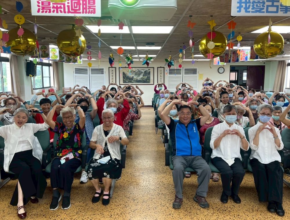 《圖說》八德榮家副主任程釋鋒(前排右3)與慈濟八德古箏班攜手比劃滿滿愛心。〈八德榮家提供〉