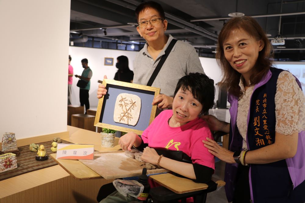 《圖說》韋汝展出自己的作品黃色小鴨和綠頭鴨及竹子，左1為指導老師張耀全  右1為八里愛心教養院院長劉文湘。〈社會局提供〉