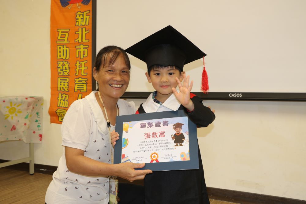 《圖說》居家托育人員為所照顧的孩子戴上方帽並致贈畢業證書。〈社會局提供〉